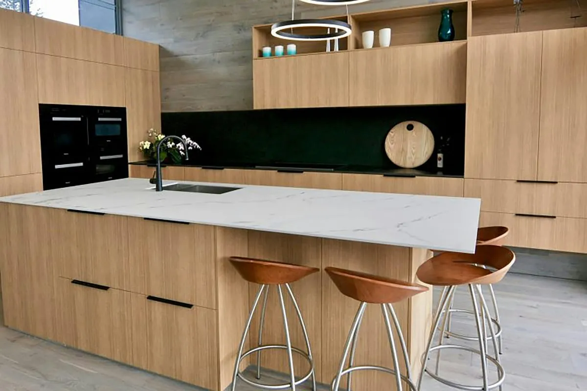 Modern custom kitchen with warm wood cabinetry, a marble waterfall island and a dark accent backsplash by Makiry Group in Sarasota, FL